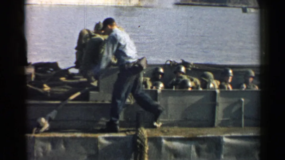 1952 Japan 8mm frame showing two men on the ferry edge with helmeted soldiers seated inside the gray craft.