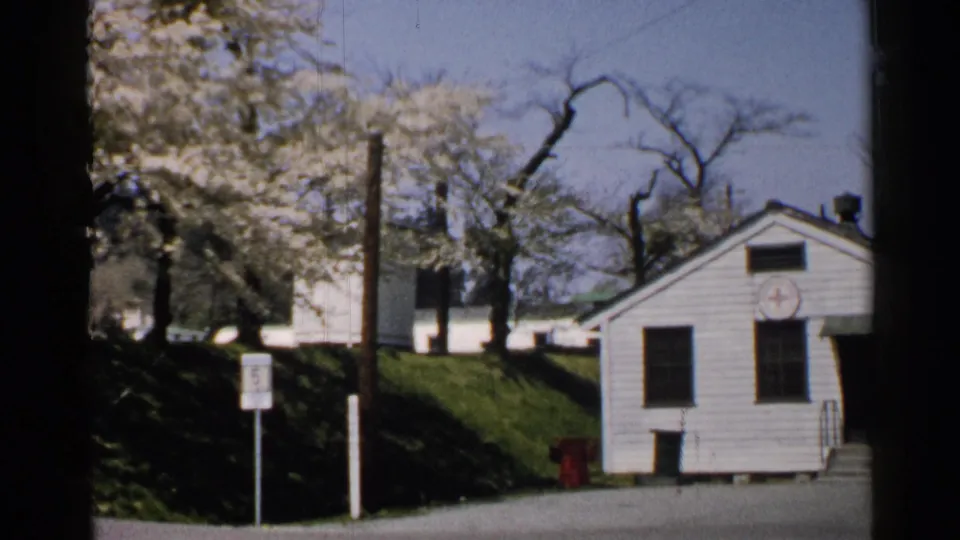 1952 Japan 8mm frame showing a small white church-like building with a red cross emblem near flowering trees, road signs, and a red hydrant.
