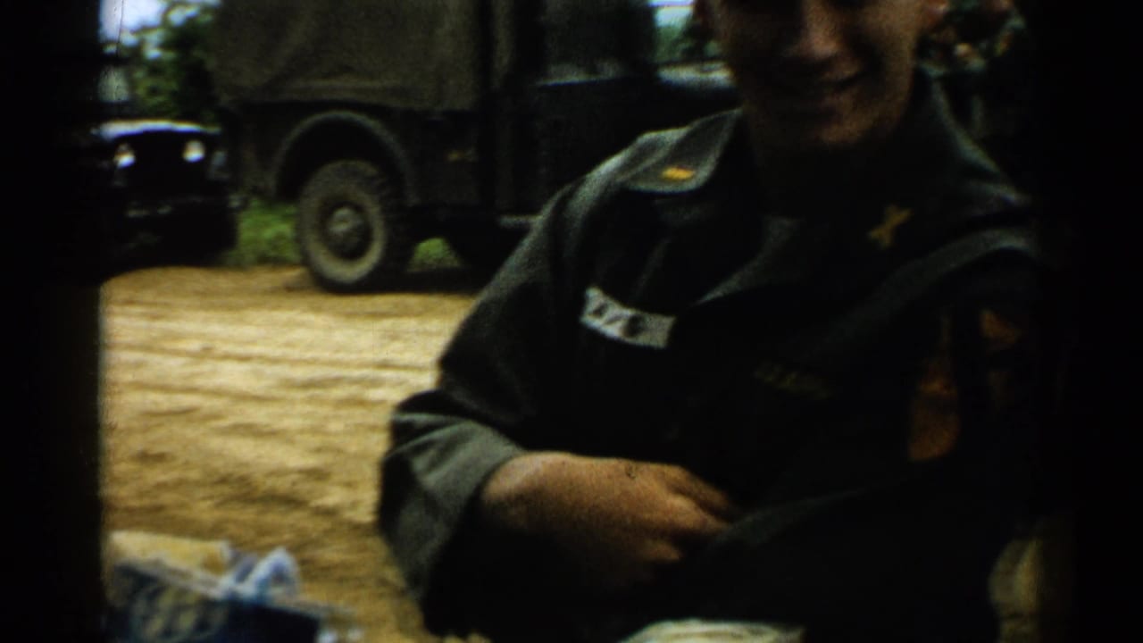 A uniformed soldier appears near the camera outdoors, with dark military vehicles parked behind him in Japan 1952 footage.