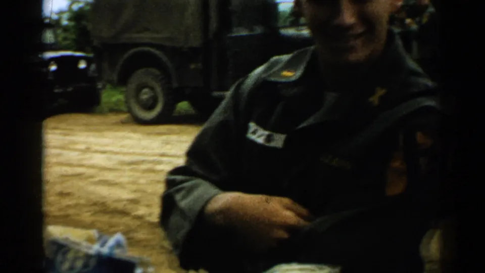 A uniformed soldier appears near the camera outdoors, with dark military vehicles parked behind him in Japan 1952 footage.