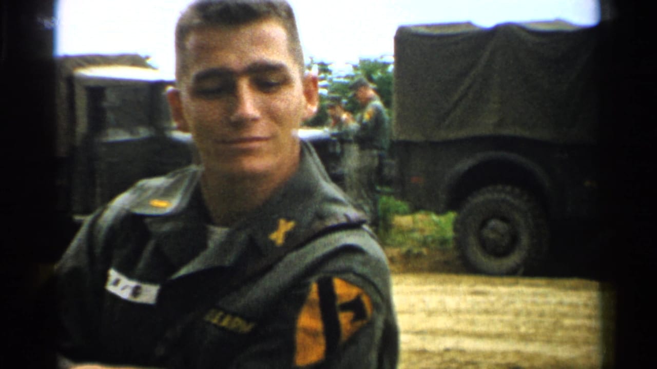 A young American soldier in 1952 Japan faces the camera in a green uniform as canvas-covered military trucks and soldiers sit behind him.