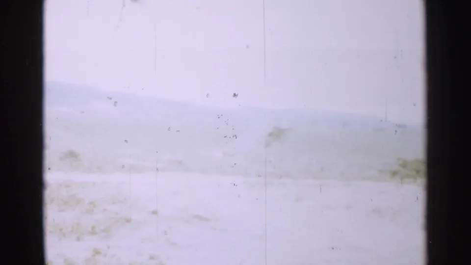 1952 Japan 8mm frame showing a pale winter landscape, faint hills, sparse brush, and heavy dark film borders.
