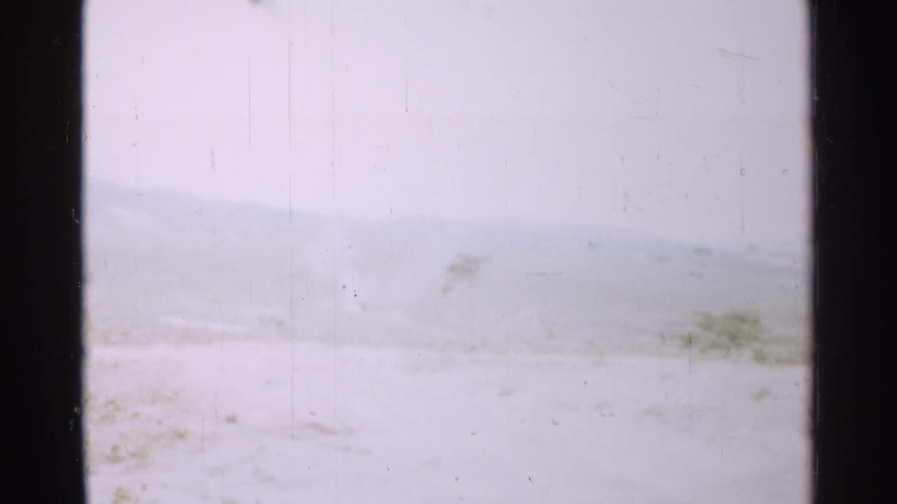 1952 Japan home-movie frame with a nearly white winter foreground, low hills, and faint vegetation softened by exposure and haze.