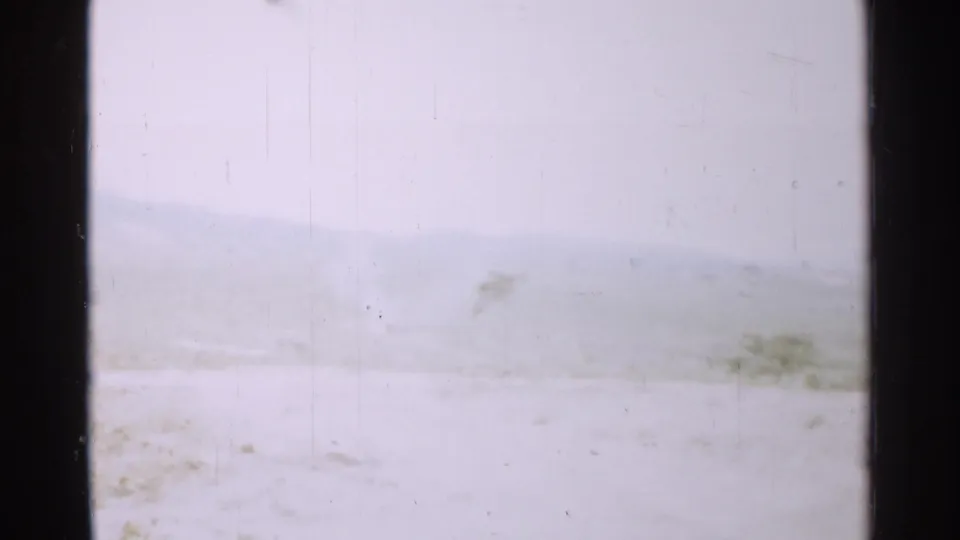 1952 Japan home-movie frame with a nearly white winter foreground, low hills, and faint vegetation softened by exposure and haze.