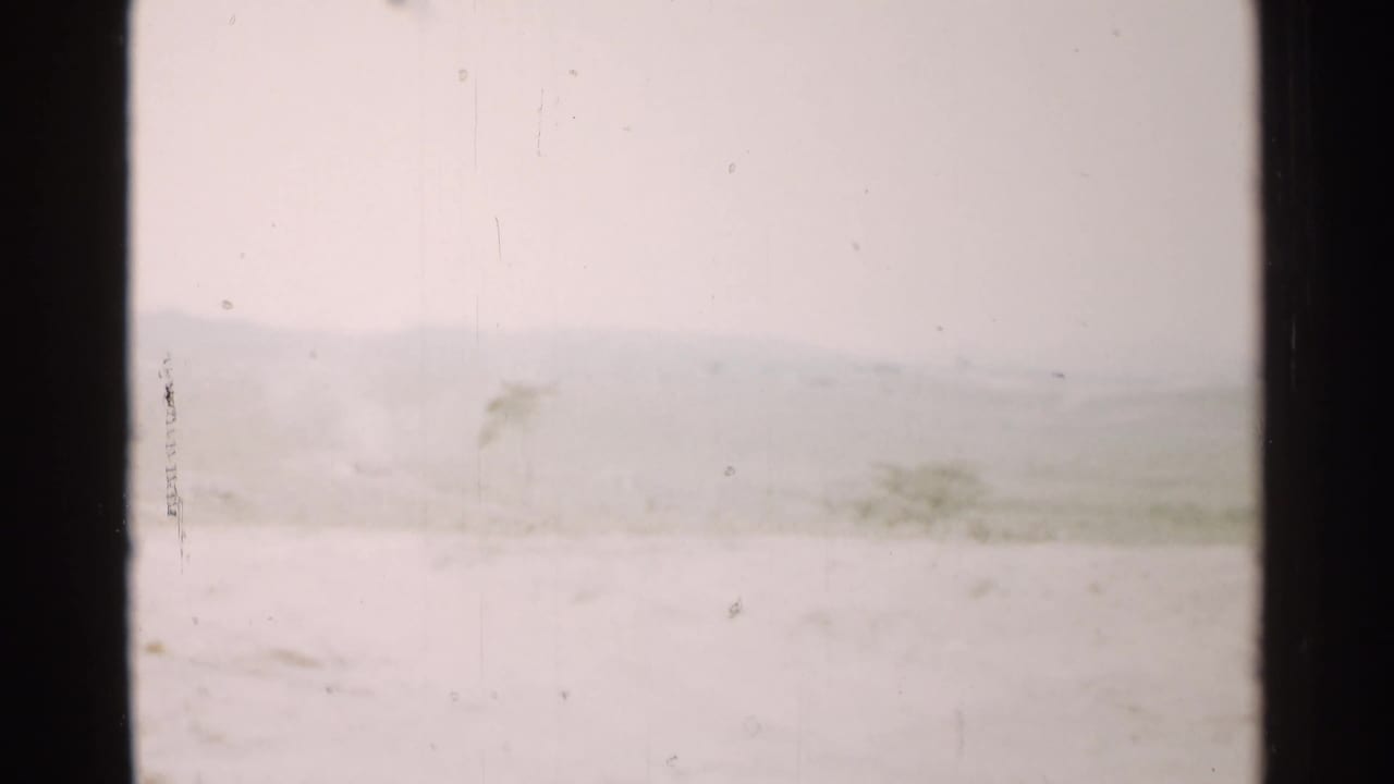 1952 Japan home-movie frame with a washed-out snowy foreground, faint hills, sparse plants, and visible 8mm surface wear.
