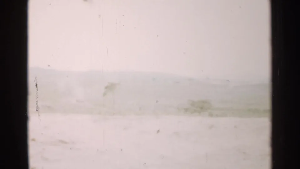 1952 Japan home-movie frame with a washed-out snowy foreground, faint hills, sparse plants, and visible 8mm surface wear.