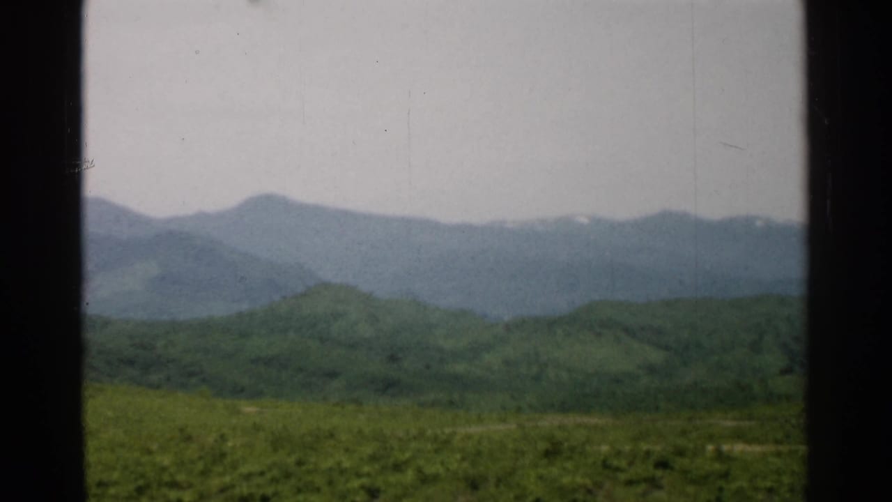 1952 Japan 8mm landscape frame with rolling green hills, distant mountain ridges, and faint white patches near the peaks.