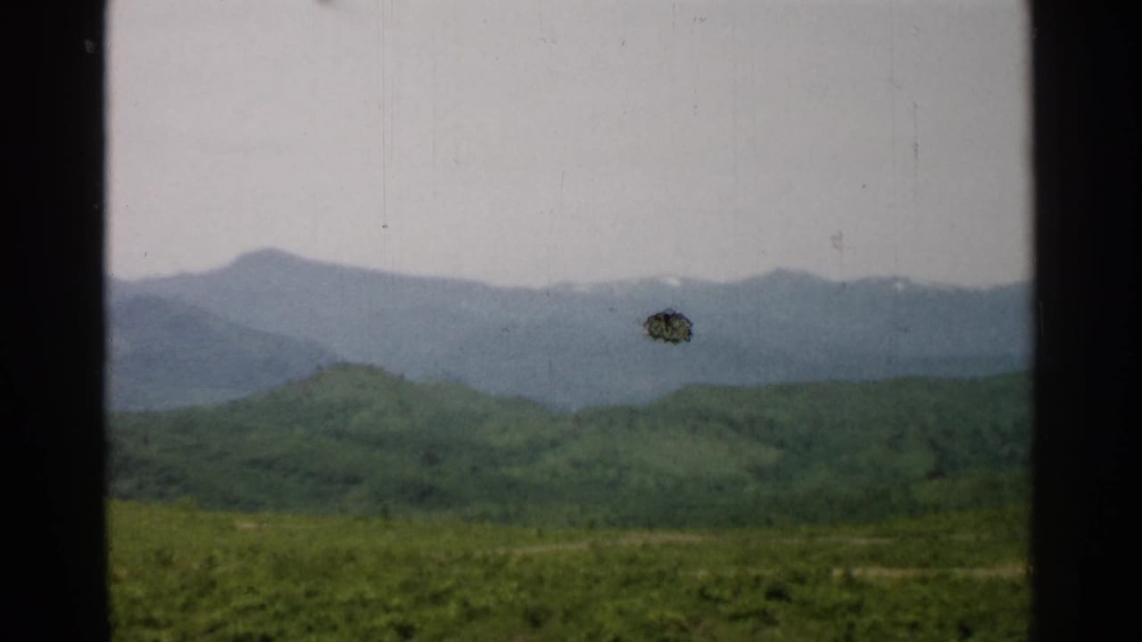 1952 Japan home-movie frame showing green hills and distant hazy mountains, with a visible dark film mark near the ridge.