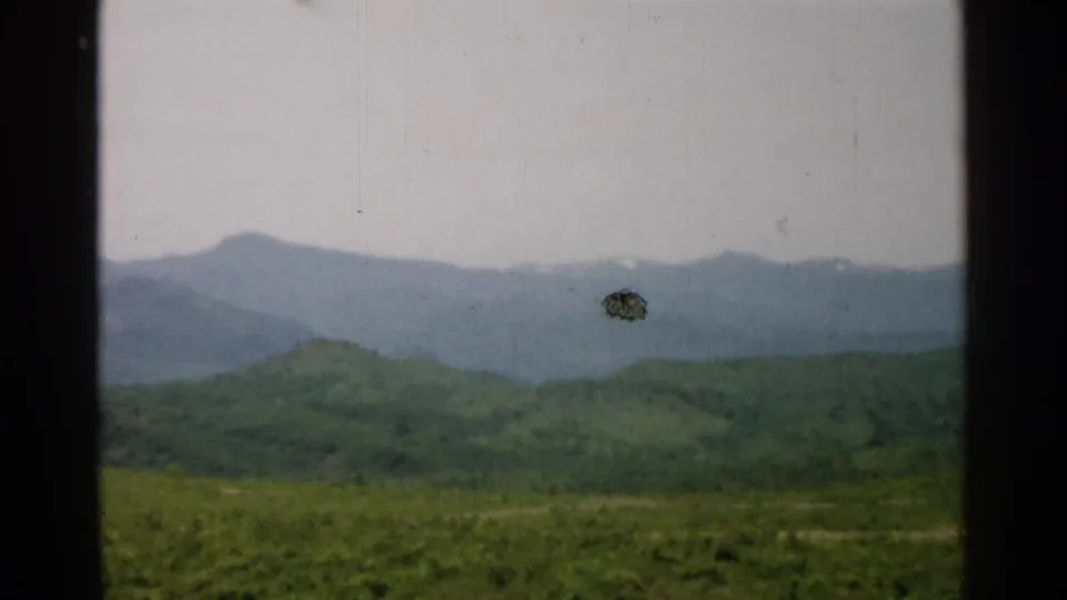1952 Japan home-movie frame showing green hills and distant hazy mountains, with a visible dark film mark near the ridge.