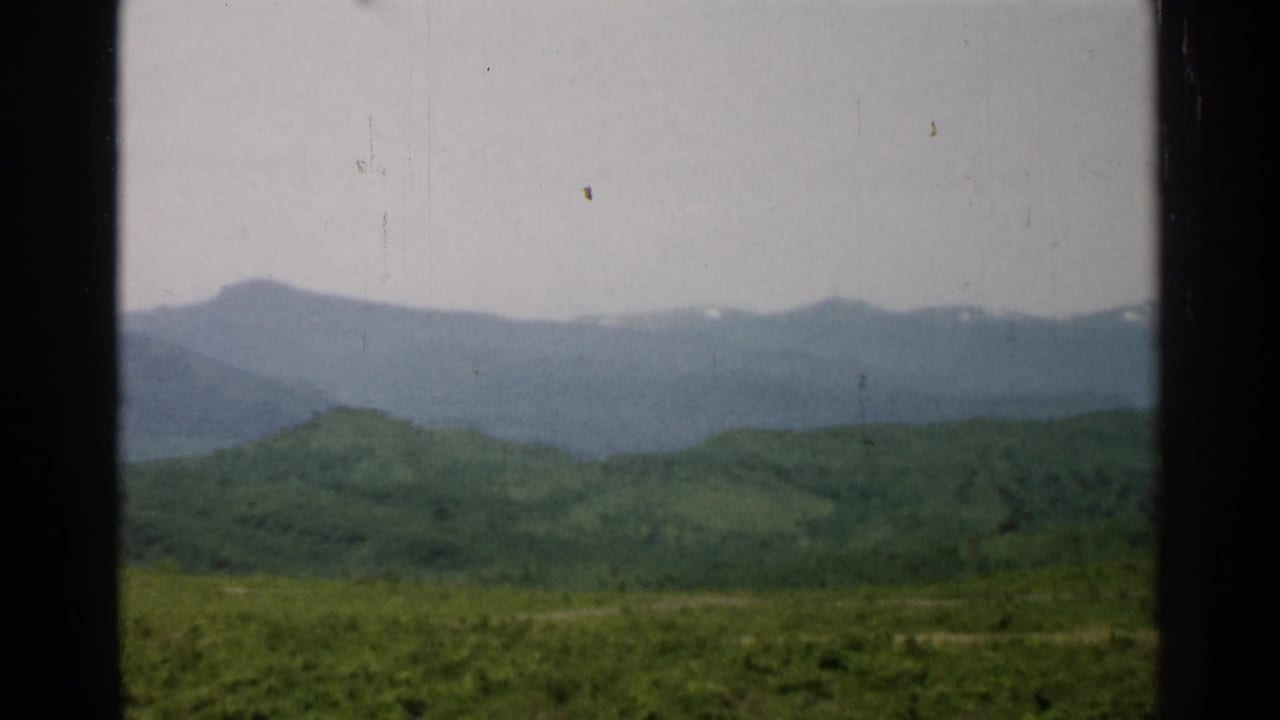 Green hills and a distant mountain range seen through dark vertical frame edges.
