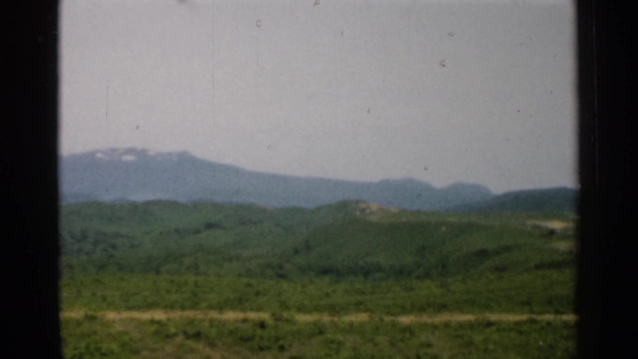 Distant mountain ridge beyond layered green hills and open grassland.