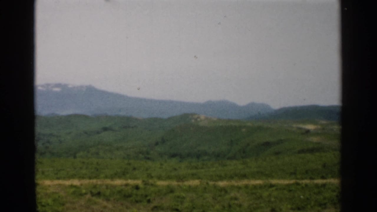 1952 Japan 8mm frame showing a green rural hillside foreground and distant blue mountains in soft focus.