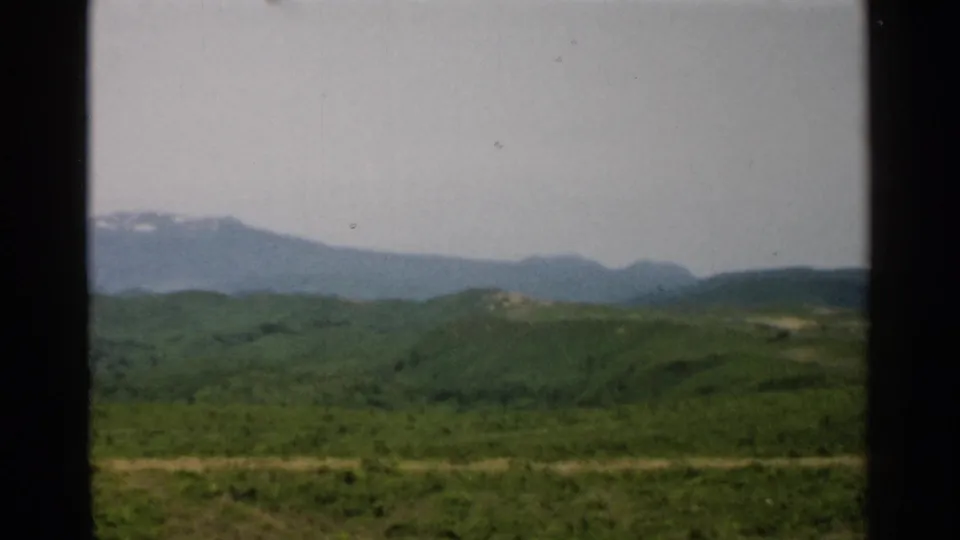 1952 Japan 8mm frame showing a green rural hillside foreground and distant blue mountains in soft focus.
