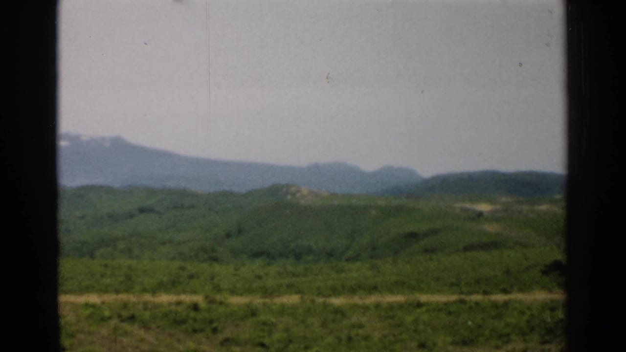 1952 Japan home-movie frame showing open green hills, a hazy mountain range, and bright subdued daylight.