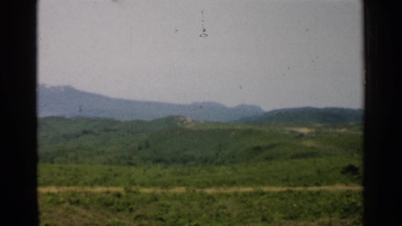 Green hills, a dirt road, and distant mountains seen through dark window-frame edges.