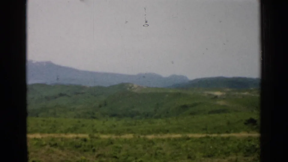 1952 Japan home-movie view of green countryside, a pale road, and distant mountains framed by a dark window edge.