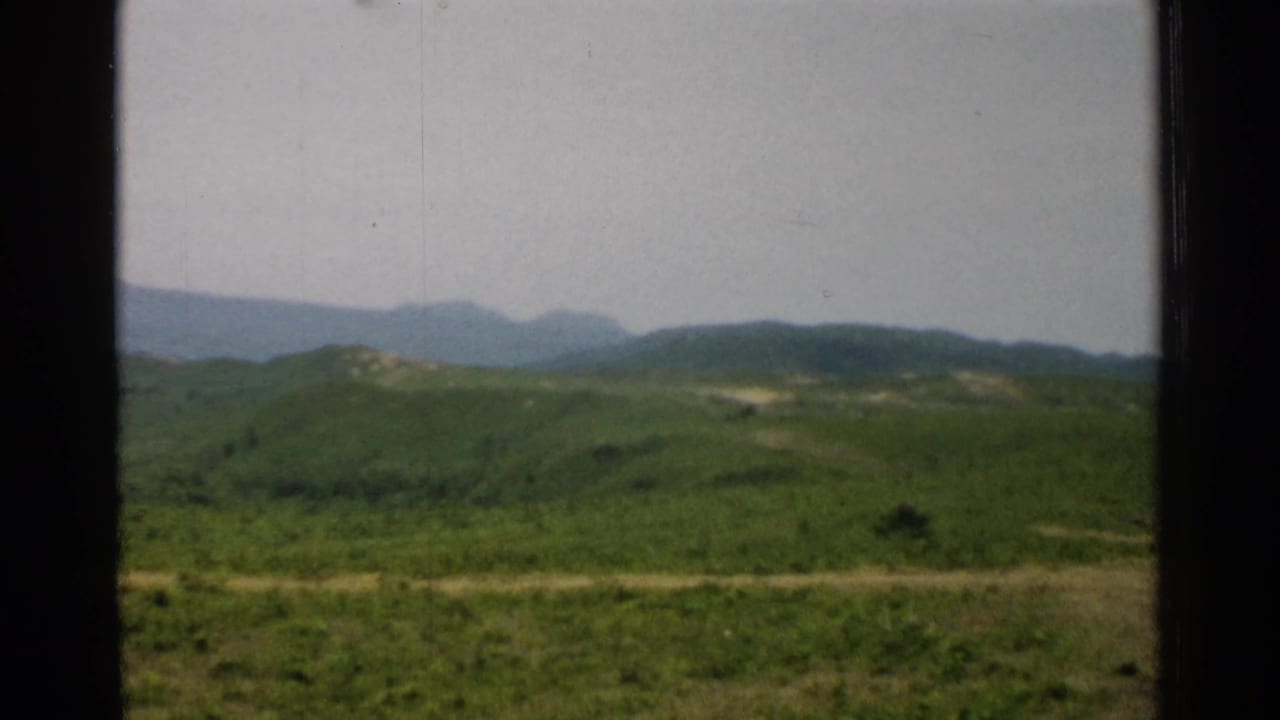 Rolling green hills and distant mountains seen through dark vertical frame bars.