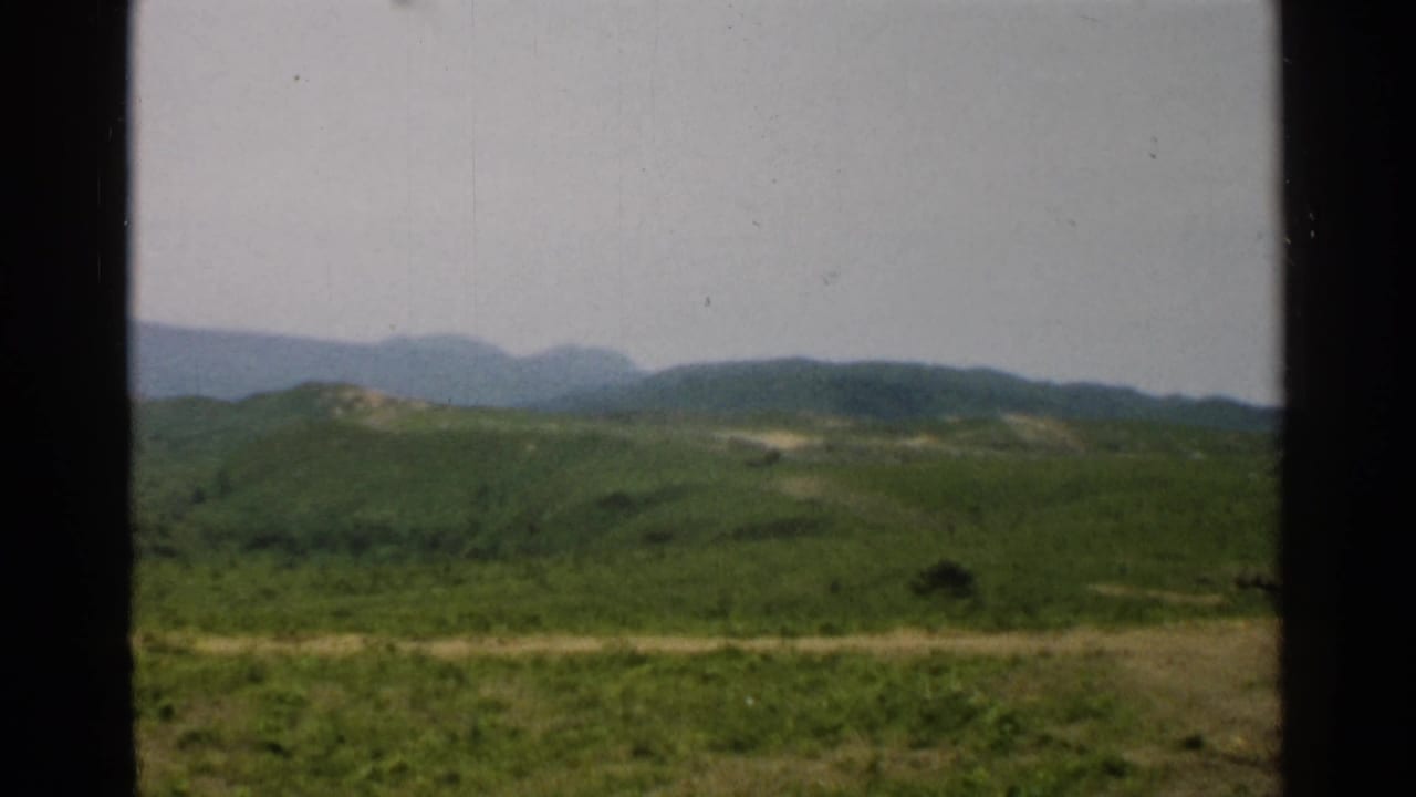 1952 Japan 8mm landscape with a soft mountain ridge beyond green hills and dark framing at the sides.