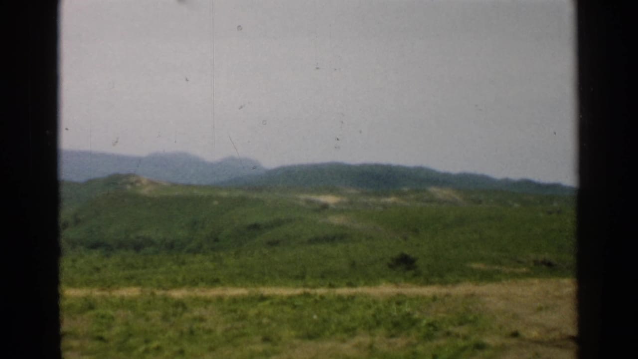1952 Japan 8mm frame showing grassy foreground, rolling hills, distant mountains, and dark vertical bars.