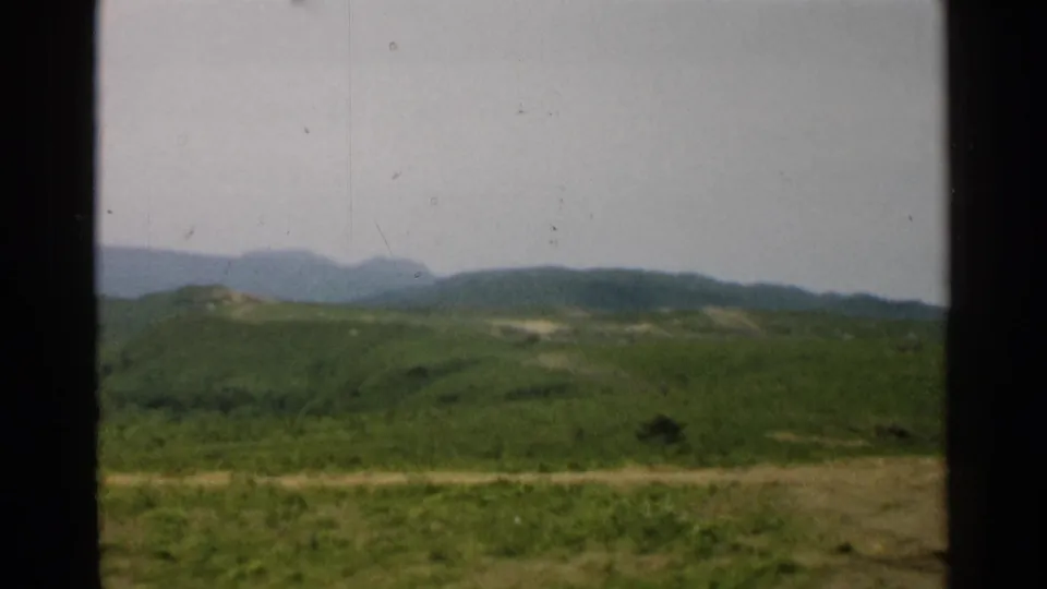 1952 Japan 8mm frame showing grassy foreground, rolling hills, distant mountains, and dark vertical bars.