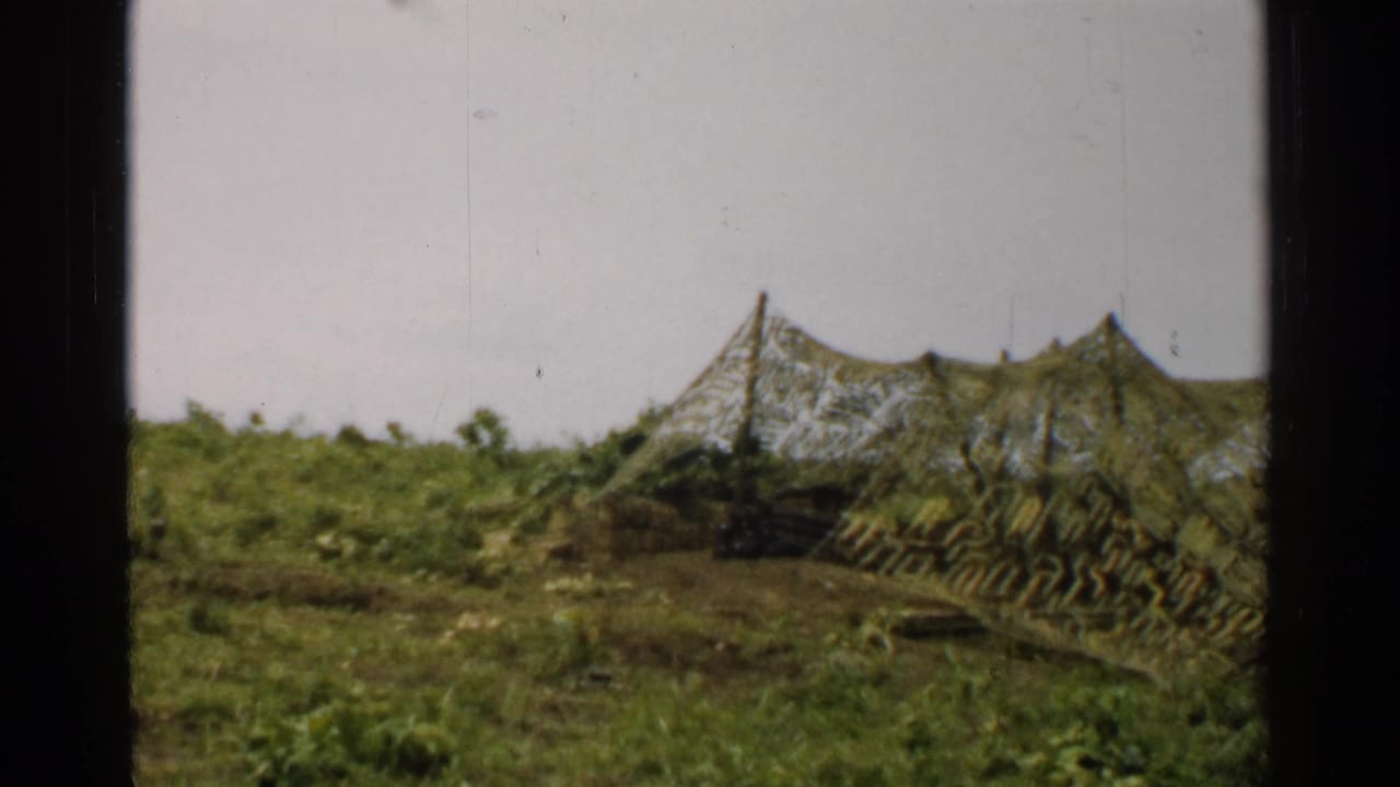 1952 Japan 8mm view of a camouflaged-looking structure set among low vegetation and hillside terrain.