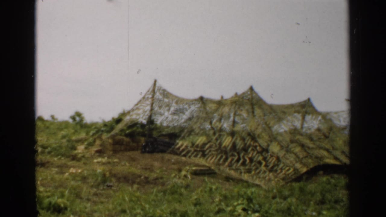 1952 Japan 8mm view of a green and brown camouflaged tent or cover blending into surrounding grass and shrubs.
