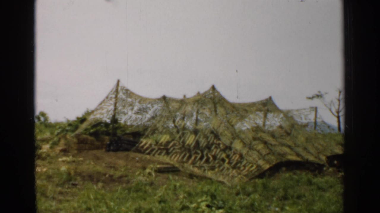 1952 Japan 8mm frame with a low camouflaged tent or netted cover in grass and a sparse tree visible near the right edge.