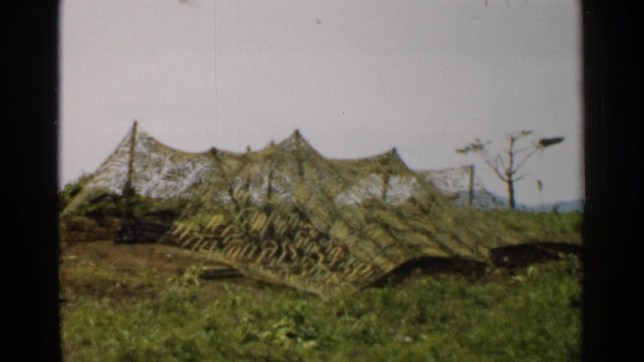 1952 Japan 8mm frame showing the camouflaged tent or cover from a slightly shifted angle in a grassy rural landscape.