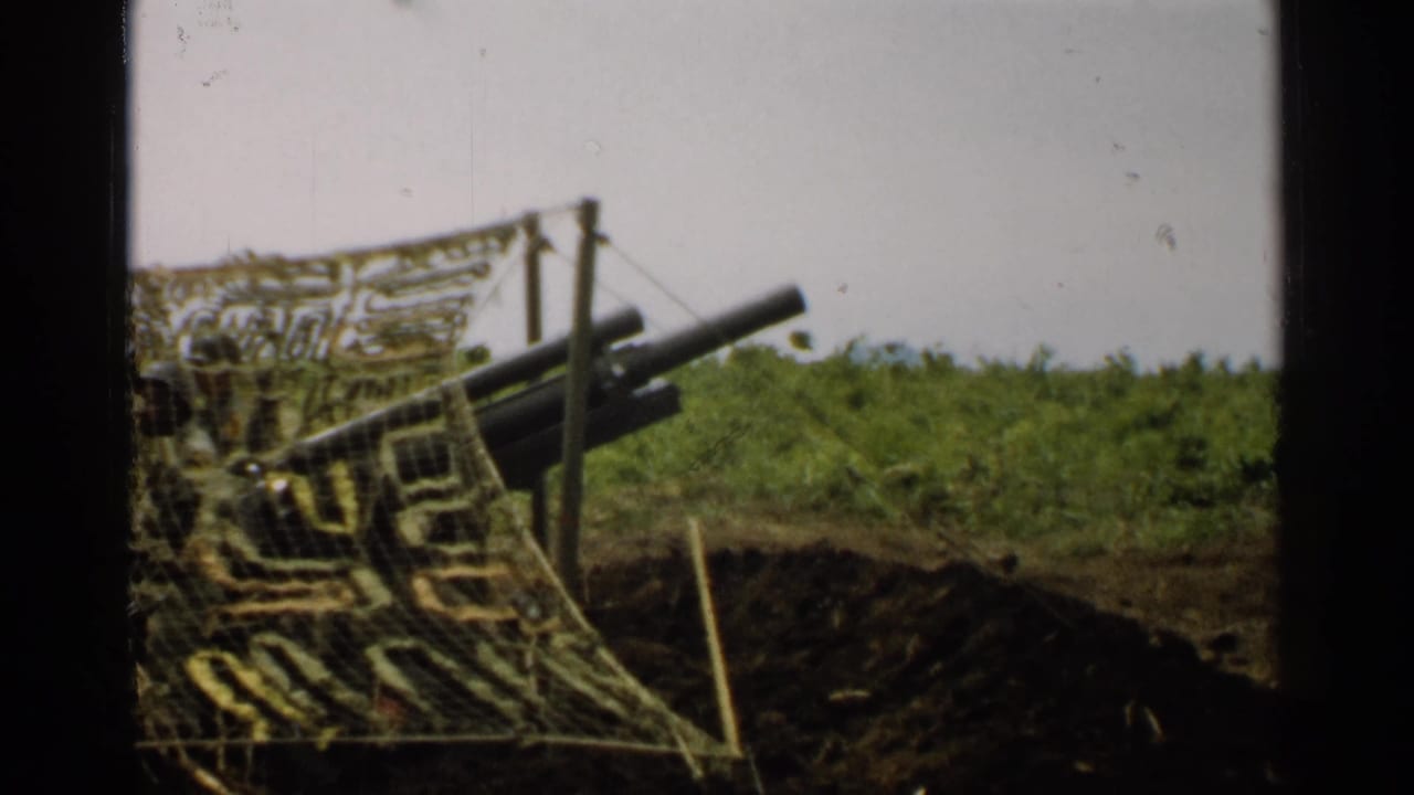1952 Japan 8mm frame showing artillery barrels protruding from a camouflaged emplacement beside a dark trench or dugout in grass.