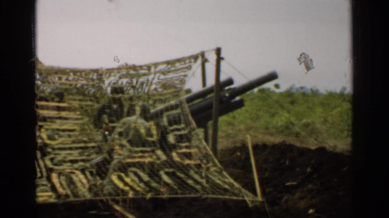 1952 Japan 8mm frame with a closer view of camouflage netting, artillery barrels, posts, foliage, and earthworks.
