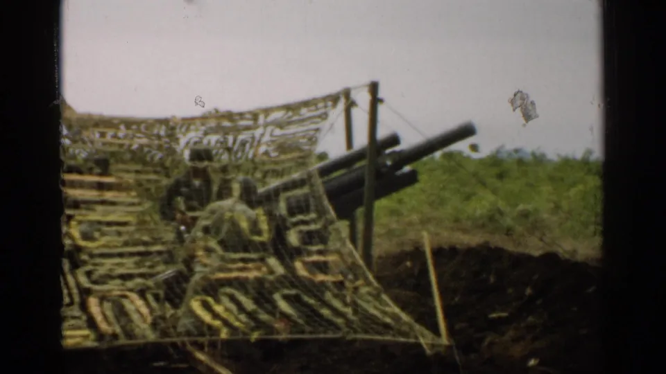 1952 Japan 8mm frame with a closer view of camouflage netting, artillery barrels, posts, foliage, and earthworks.