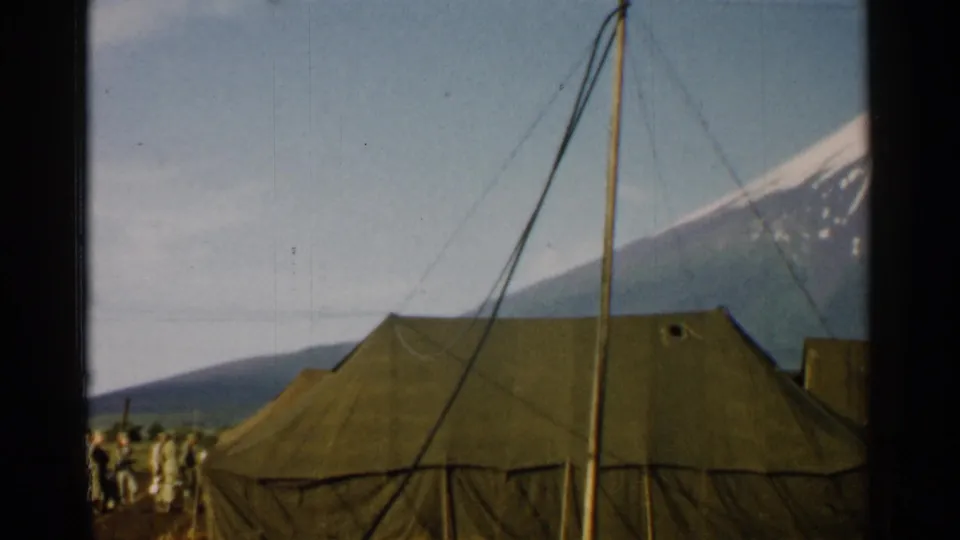 1952 Japan home-movie frame showing olive canvas tents, support poles, distant uniformed figures, and snow-capped Mount Fuji.