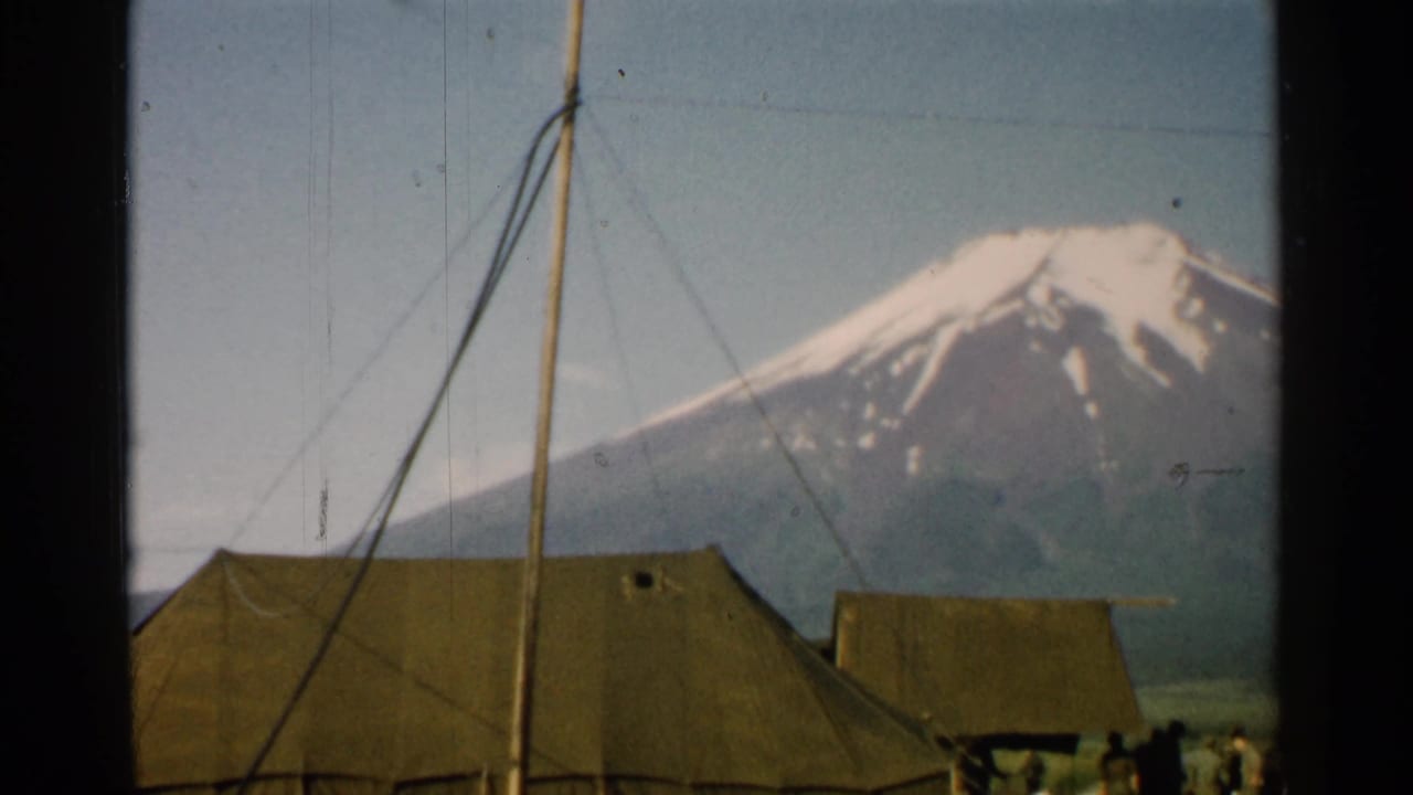 1952 Japan home-movie frame showing tents, pole rigging, people near the camp edge, and Mount Fuji under a clear sky.