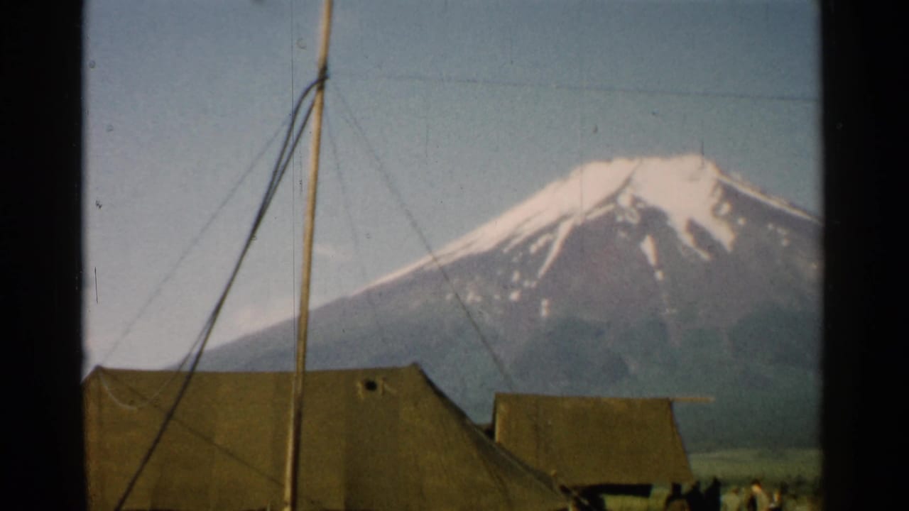 Mount Fuji behind canvas tents, a tall pole, and guy wires under a pale sky.