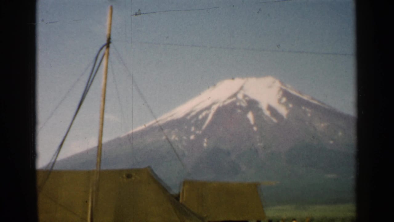 Snow-capped mountain seen beyond canvas tents, guy wires, and a tall pole.