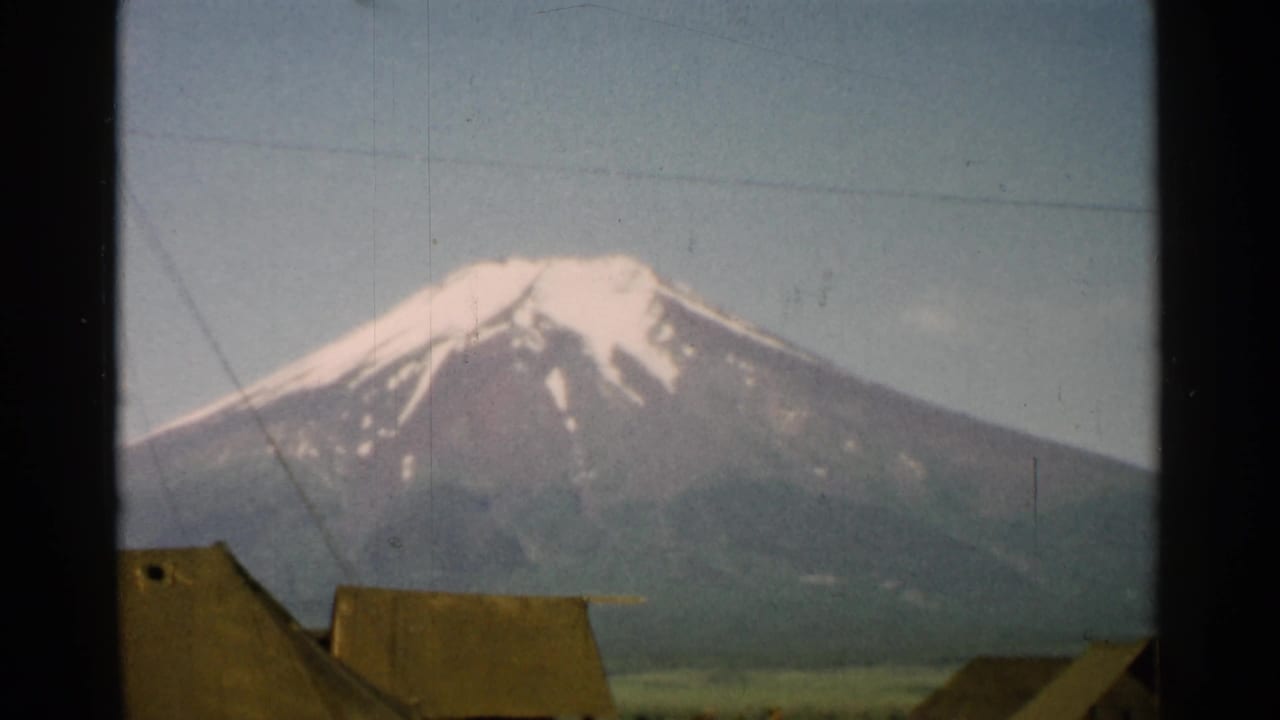 Snow-capped Mount Fuji behind thatched rooftops, seen through dark window framing.