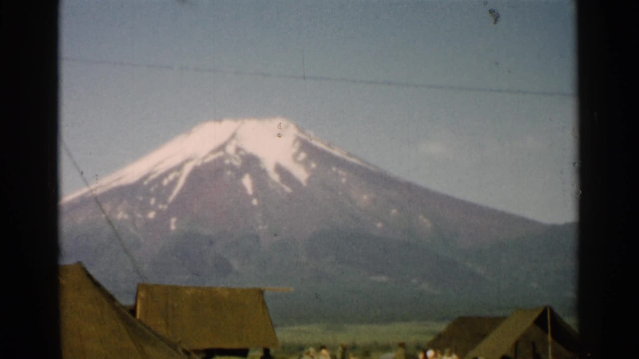 1952 Japan 8mm view of Mount Fuji above a rural village, with rooflines and small distant figures near the lower edge.