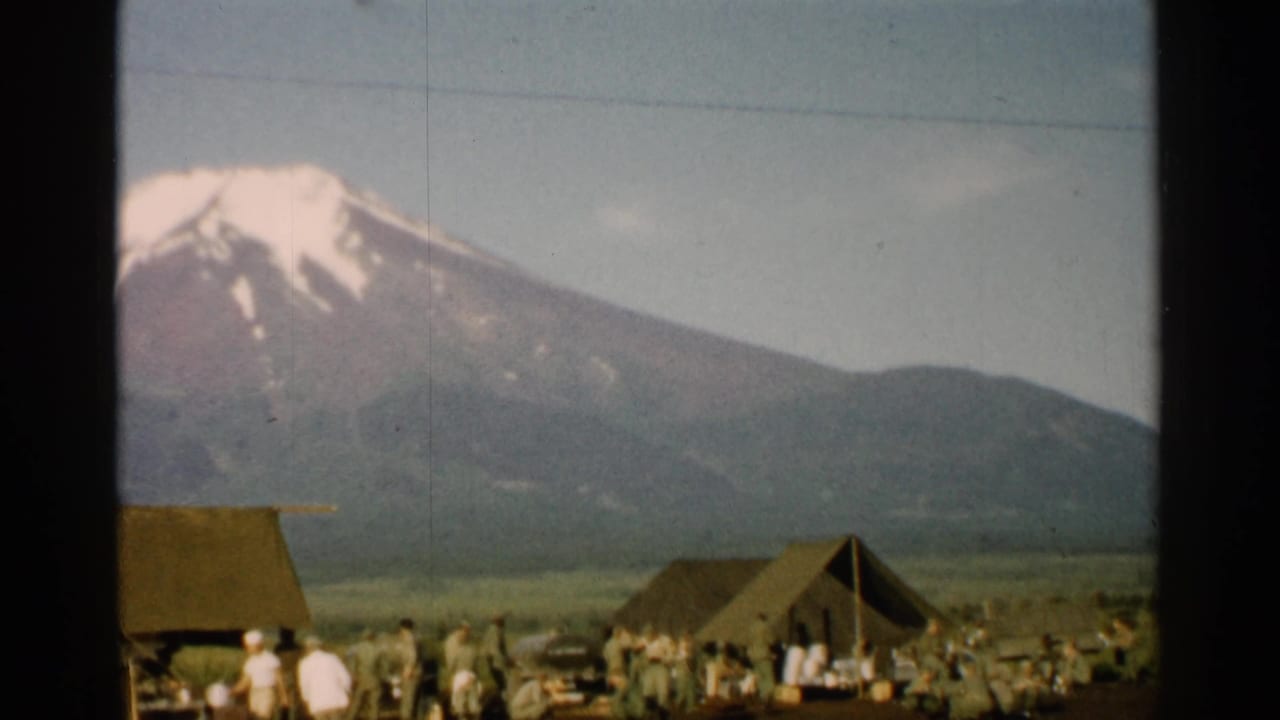 1952 Japan home-movie frame showing Mount Fuji above a military-style tent camp with uniformed people in the foreground.