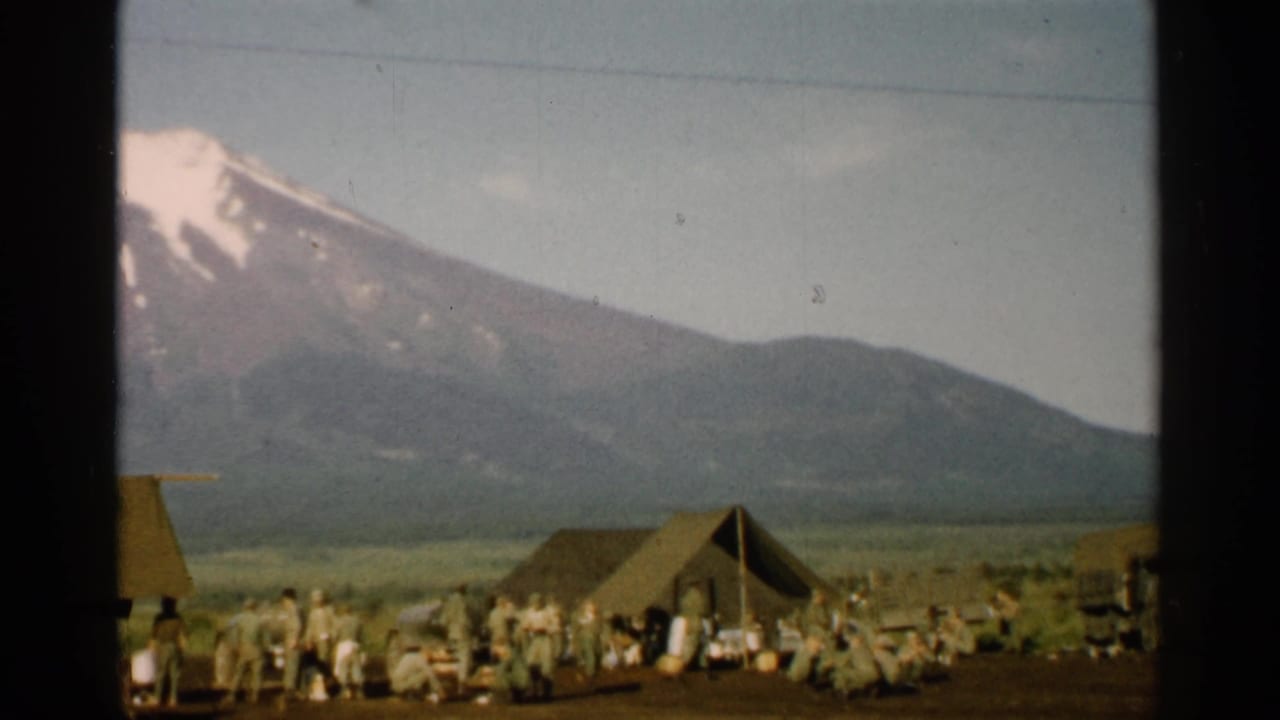 Mount Fuji and foothills overlook tents, people, and vehicles in a field camp.