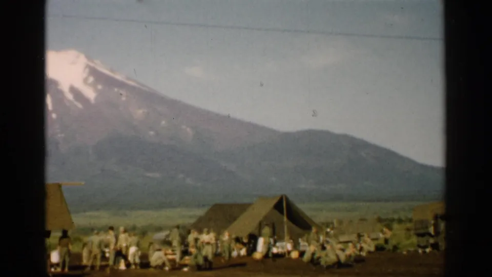 1952 Japan frame with Mount Fuji in the background and a spread of tents, personnel, gear, and vehicles across an open camp.