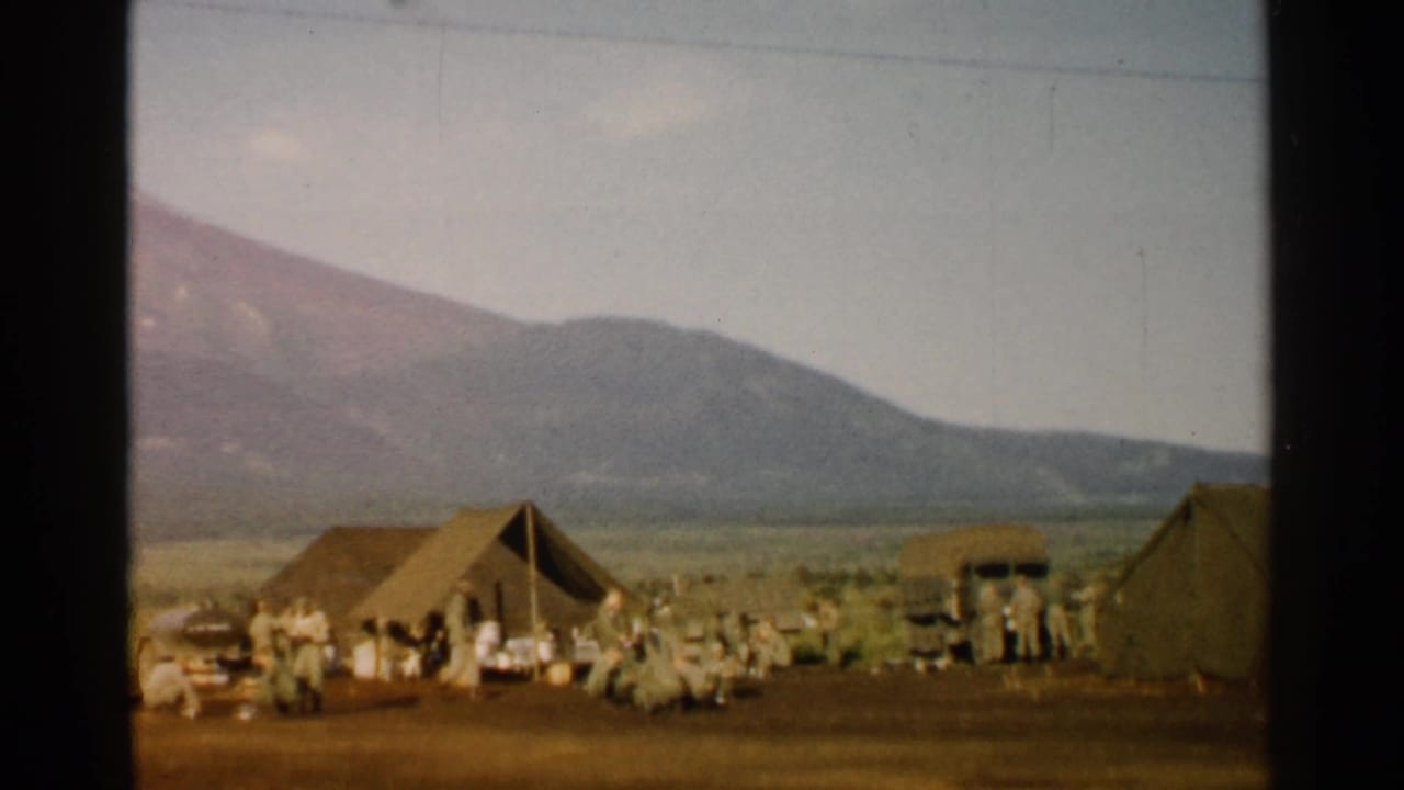 1952 Japan 8mm frame showing soldiers around canvas tents in a broad field below distant mountains.