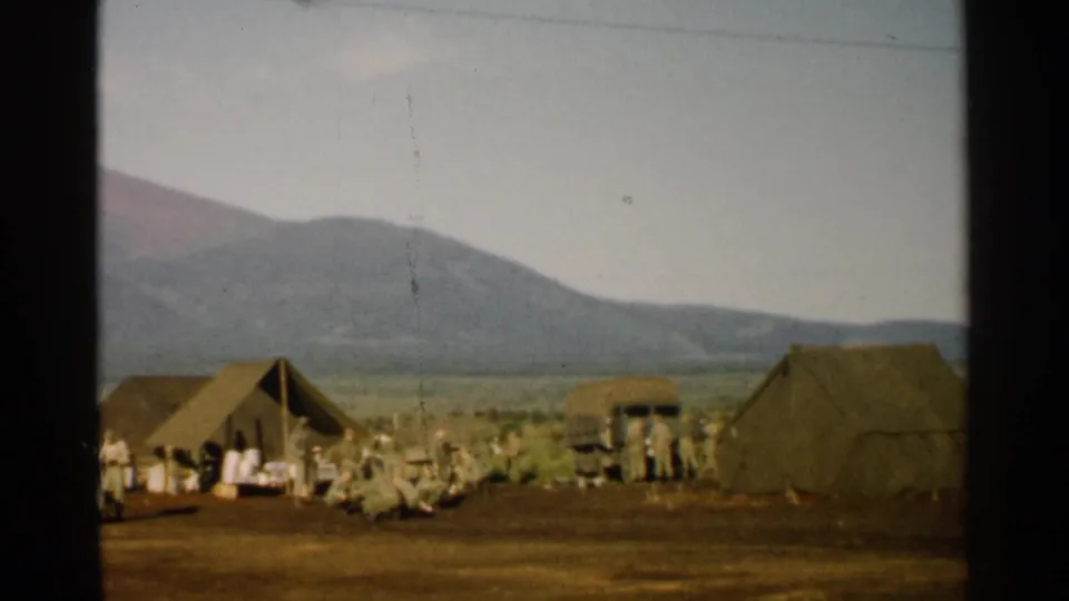 1952 Japan 8mm frame with uniformed personnel, tents, and a military truck in a mountain field camp.