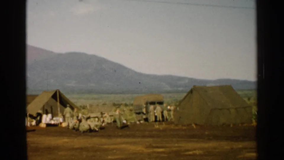 1952 Japan 8mm frame showing a wide view of a military camp with tents, soldiers, and mountains.