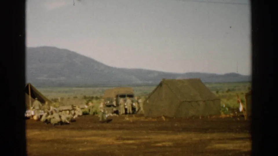1952 Japan 8mm frame with a large canvas tent, soldiers, and a truck in a mountain encampment.