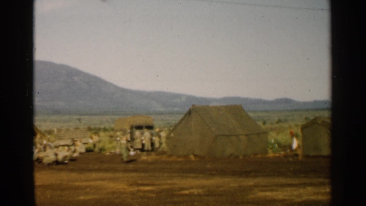1952 Japan 8mm frame showing canvas tents, a truck, open dirt ground, and distant mountains at a military camp.