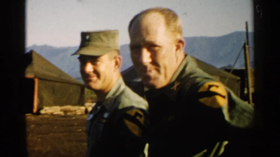 1952 Japan 8mm frame with two U.S. Army-uniformed men close to the camera, tents and mountains behind them.