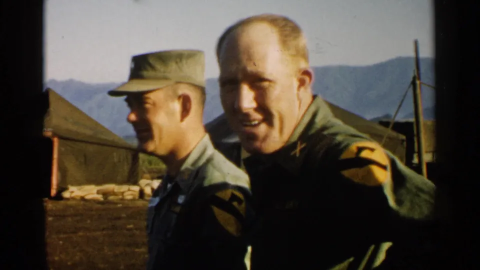 1952 Japan home-movie frame of two soldiers at a military camp, one turned in profile and one smiling near the camera.