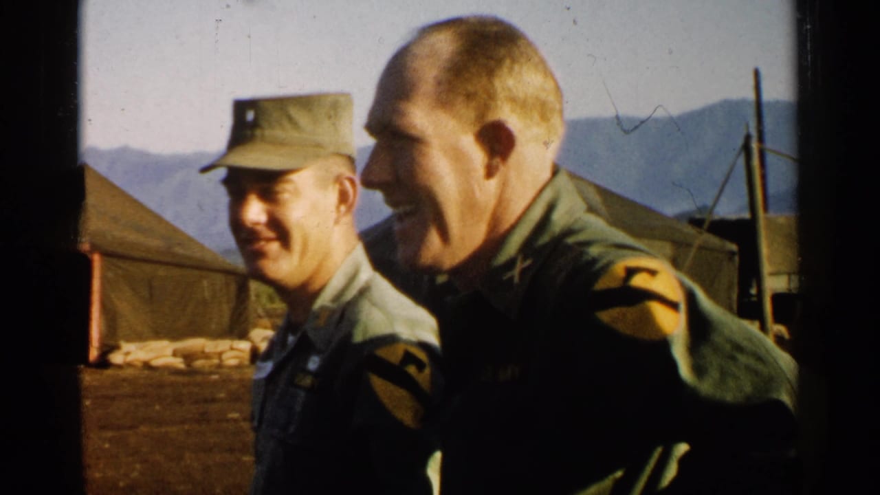 Two uniformed officers smile while standing beside camp tents.
