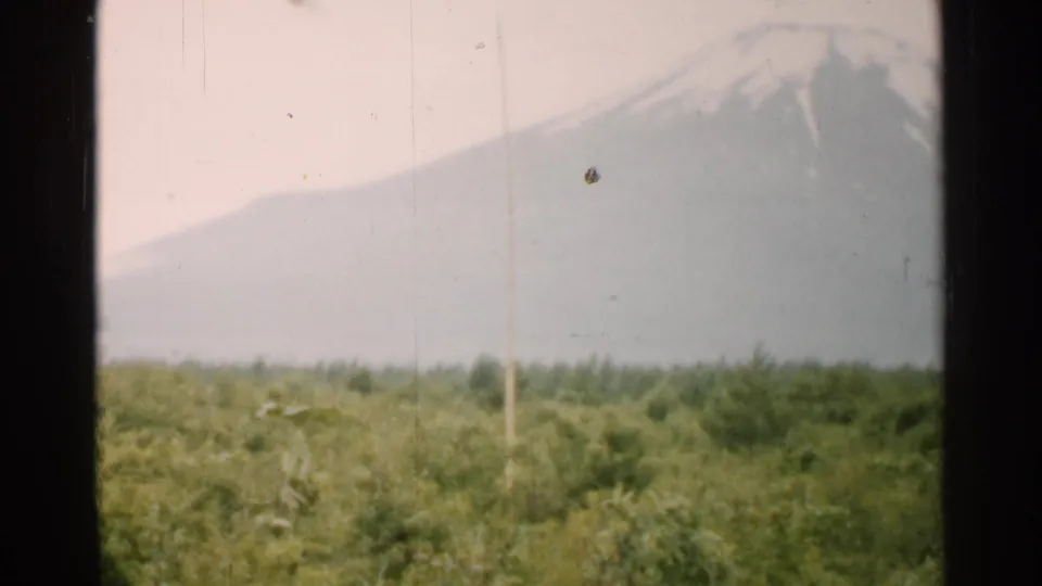 1952 Japan home-movie frame with a snowy mountain peak above forest, bordered by a dark vertical window edge.