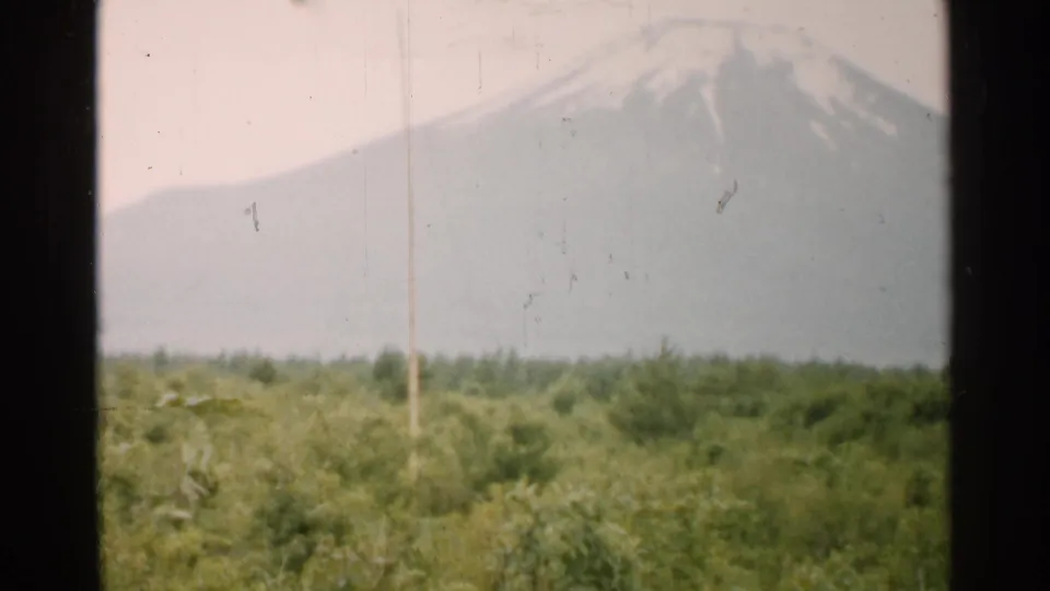 1952 Japan 8mm view of a snow-capped mountain beyond green fields, partially framed by dark vertical window edges.